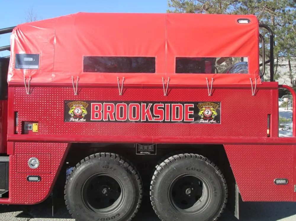Exterior view of small fire truck showing cab, body compartments, and wheel/tire area.