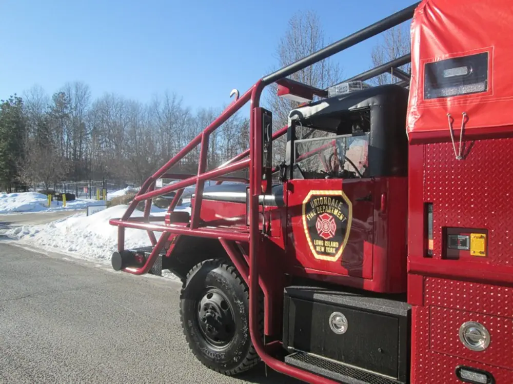 Exterior view of small fire truck showing cab, body compartments, and wheel/tire area.