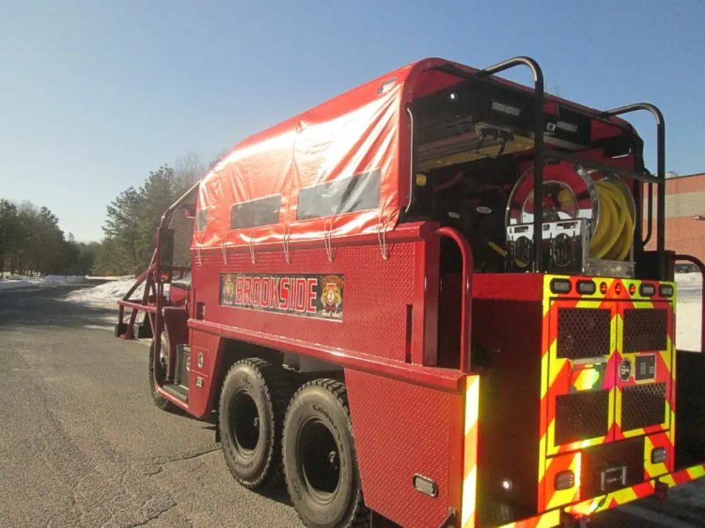 Exterior view of small fire truck showing cab, body compartments, and wheel/tire area.