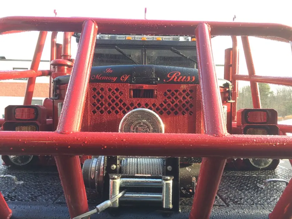 Exterior view of small fire truck showing cab, body compartments, and wheel/tire area.