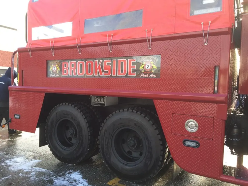 Exterior view of small fire truck showing cab, body compartments, and wheel/tire area.