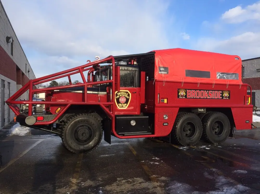 Exterior view of small fire truck showing cab, body compartments, and wheel/tire area.