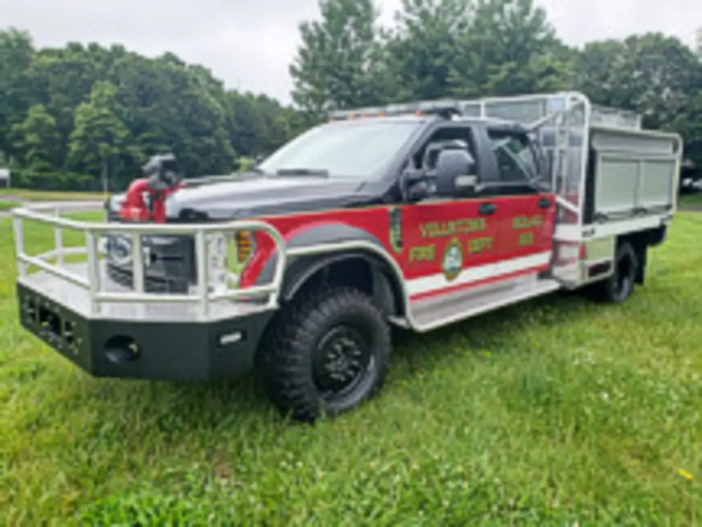 Exterior view of small fire truck showing cab, body compartments, and wheel/tire area.