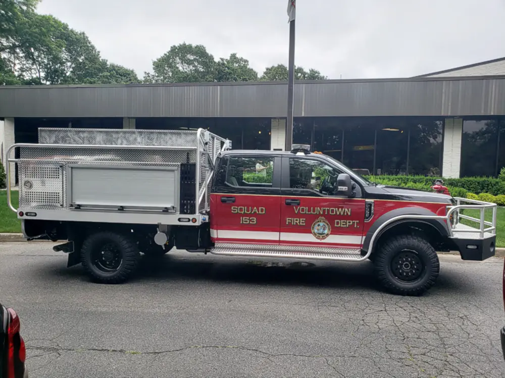 Exterior view of small fire truck showing cab, body compartments, and wheel/tire area.