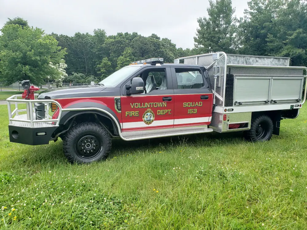 Exterior view of small fire truck showing cab, body compartments, and wheel/tire area.