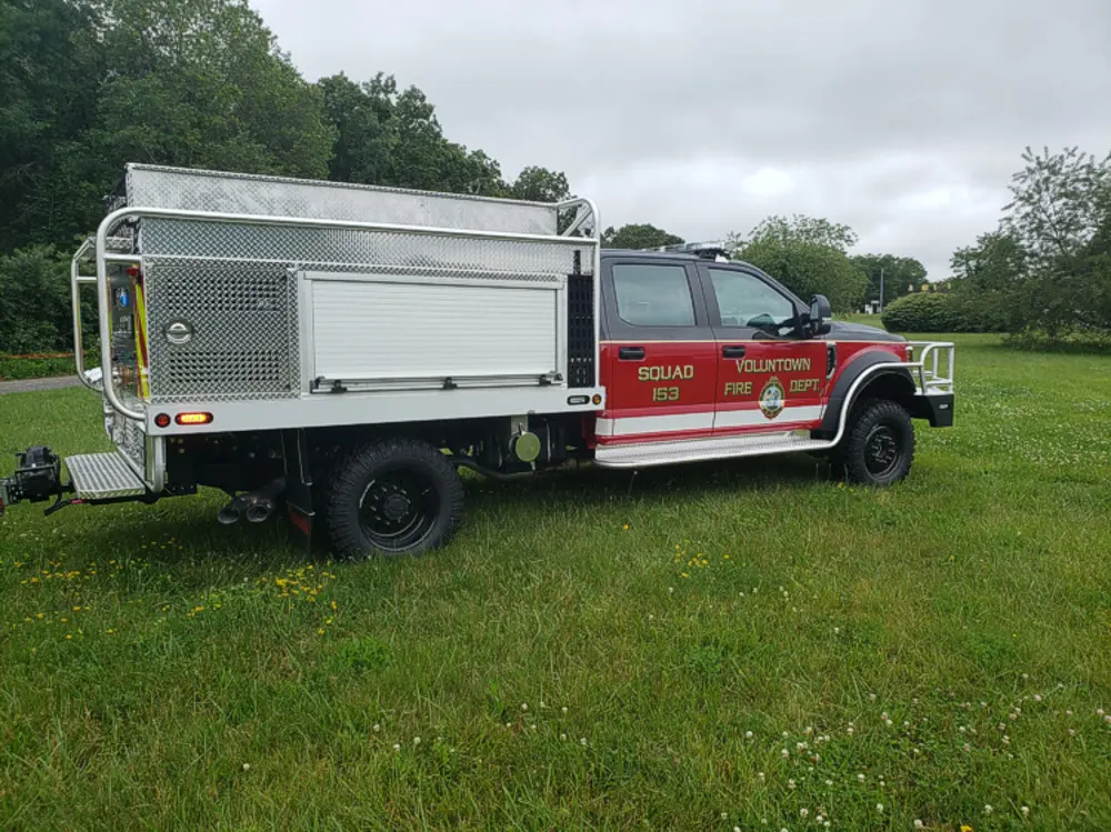 Exterior view of small fire truck showing cab, body compartments, and wheel/tire area.