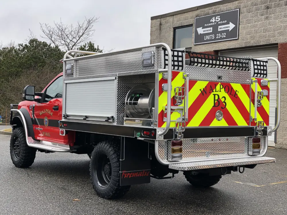 Exterior view of small fire truck showing cab, body compartments, and wheel/tire area.