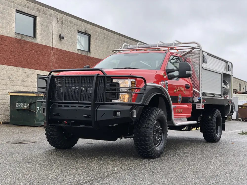 Exterior view of small fire truck showing cab, body compartments, and wheel/tire area.