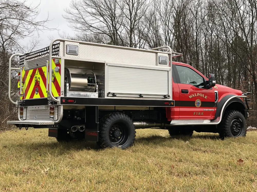Exterior view of small fire truck showing cab, body compartments, and wheel/tire area.