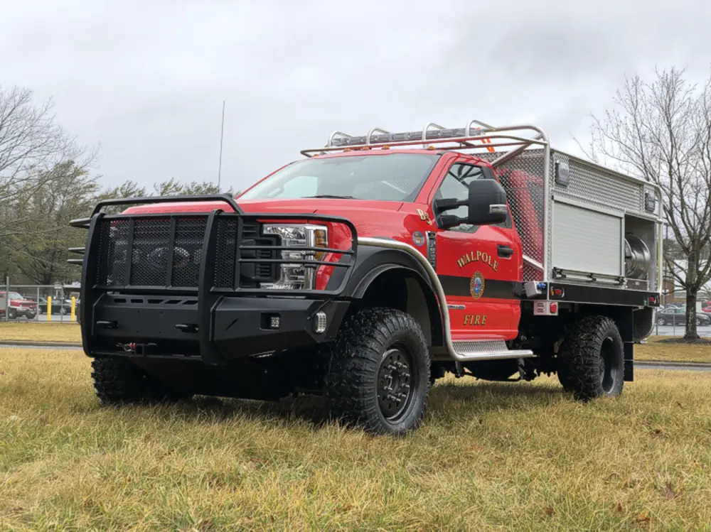 Exterior view of small fire truck showing cab, body compartments, and wheel/tire area.