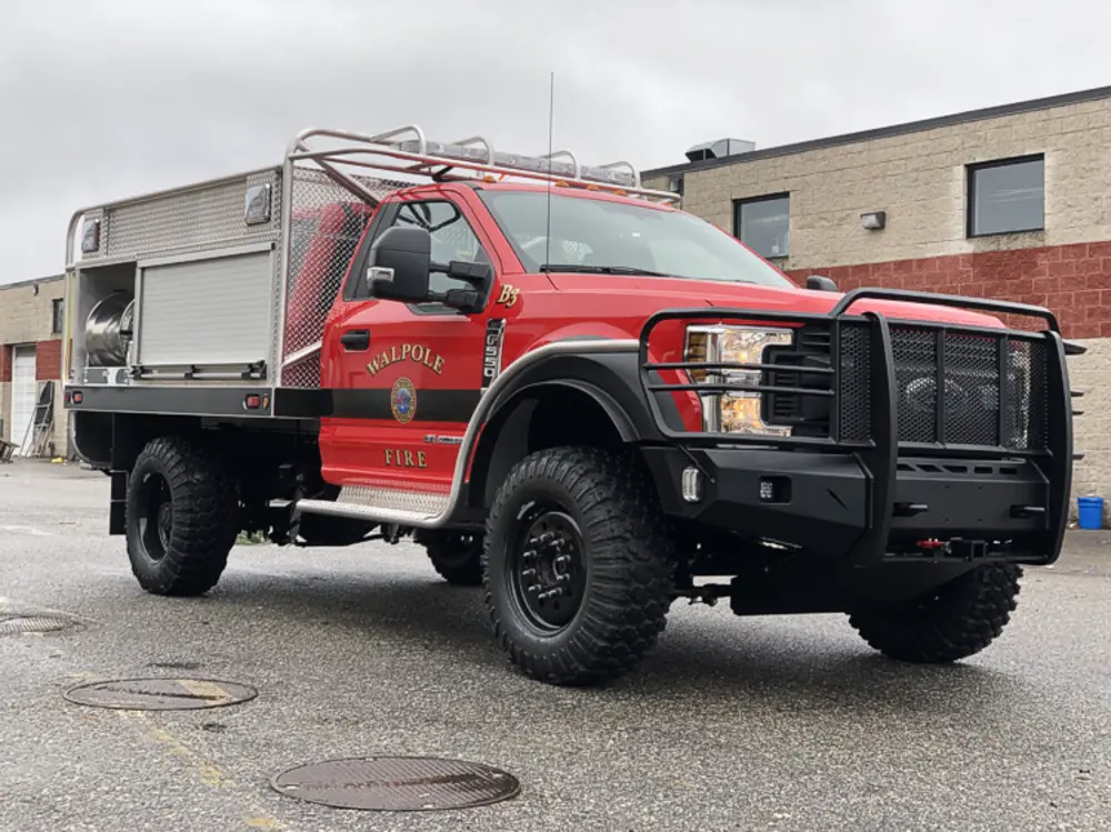Exterior view of small fire truck showing cab, body compartments, and wheel/tire area.