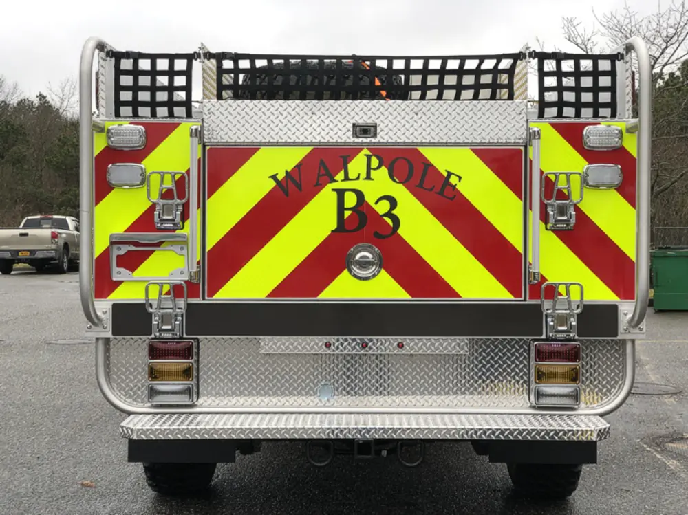 Exterior view of small fire truck showing cab, body compartments, and wheel/tire area.