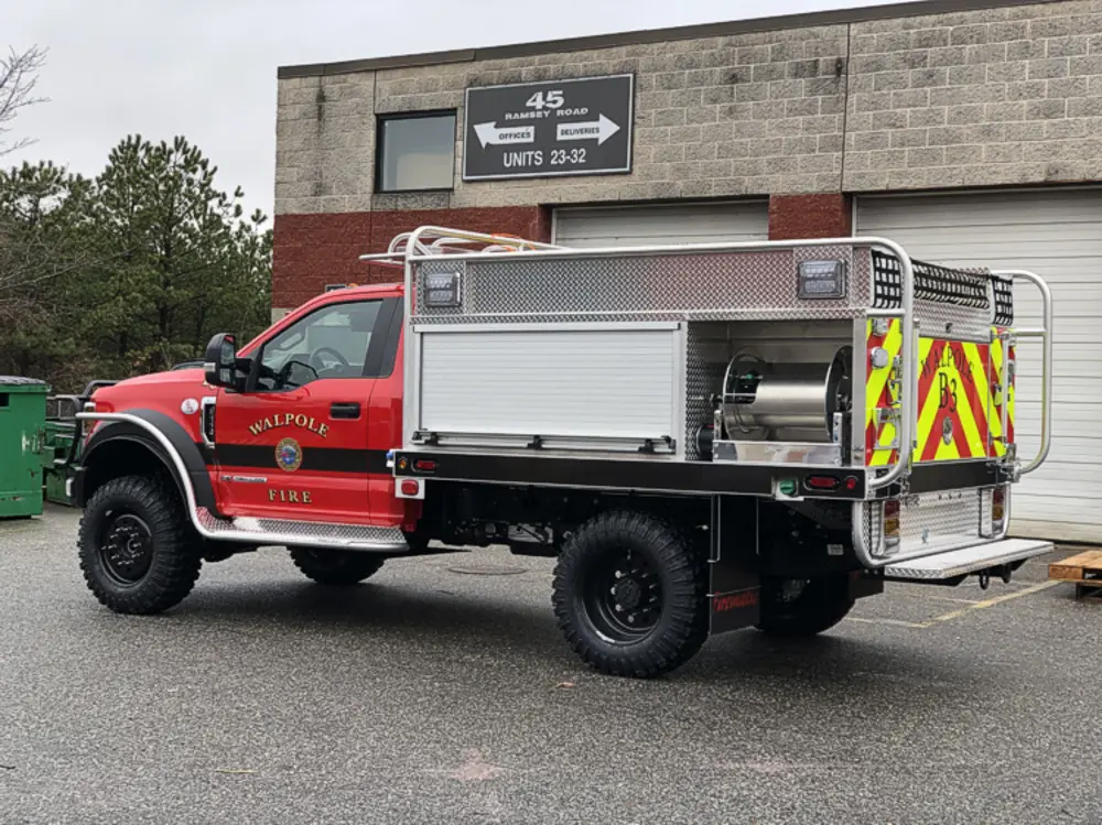 Exterior view of small fire truck showing cab, body compartments, and wheel/tire area.