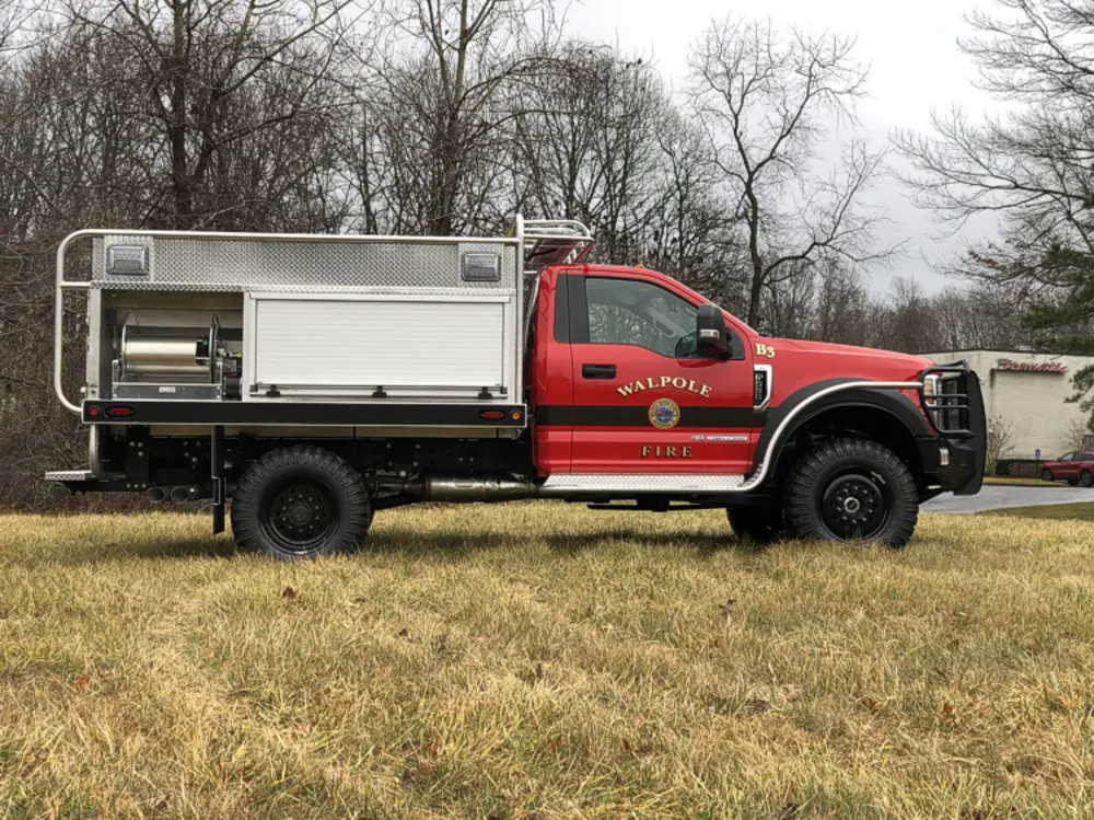 Exterior view of small fire truck showing cab, body compartments, and wheel/tire area.