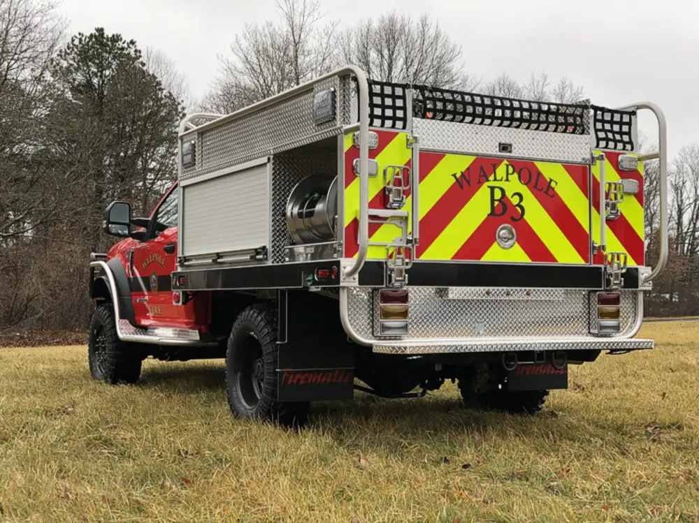 Exterior view of small fire truck showing cab, body compartments, and wheel/tire area.