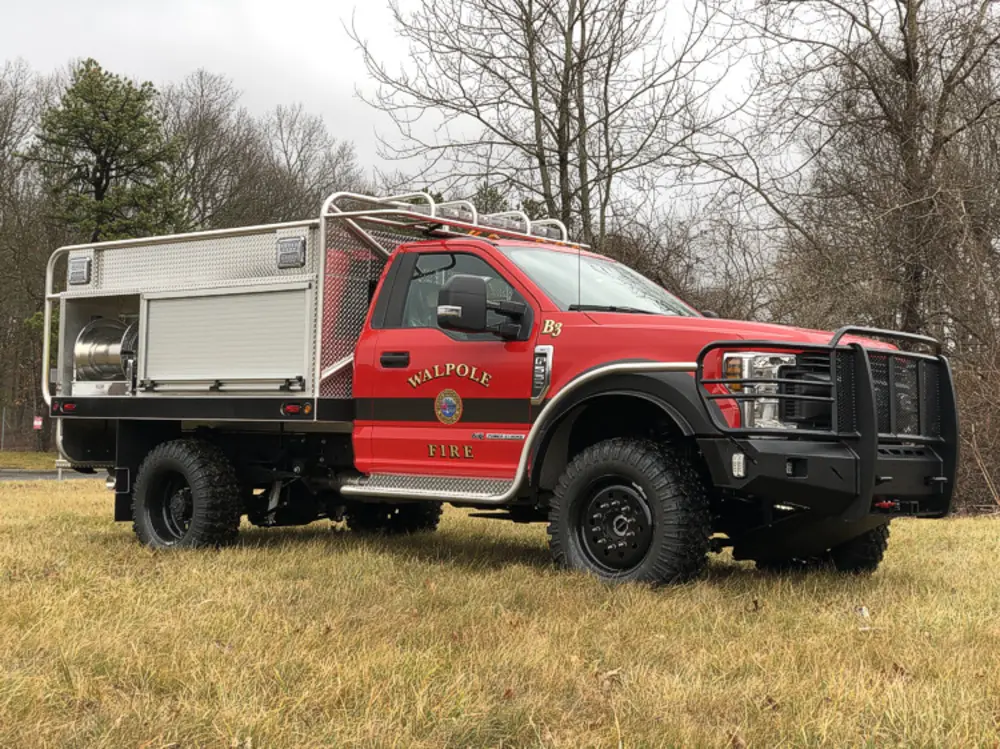 Exterior view of small fire truck showing cab, body compartments, and wheel/tire area.