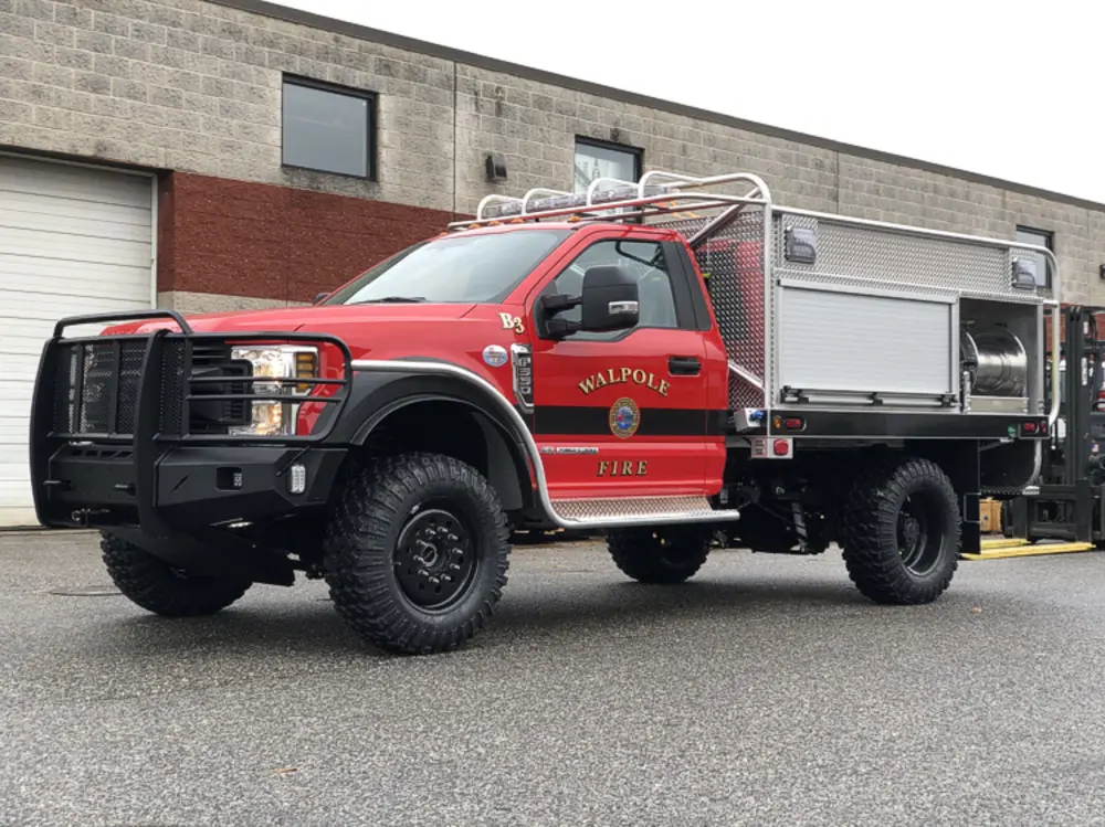 Exterior view of small fire truck showing cab, body compartments, and wheel/tire area.
