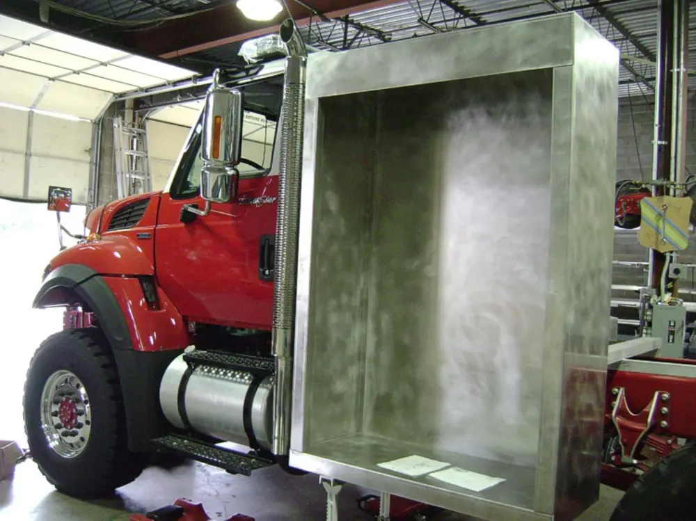 Exterior view of small fire truck showing cab, body compartments, and wheel/tire area.