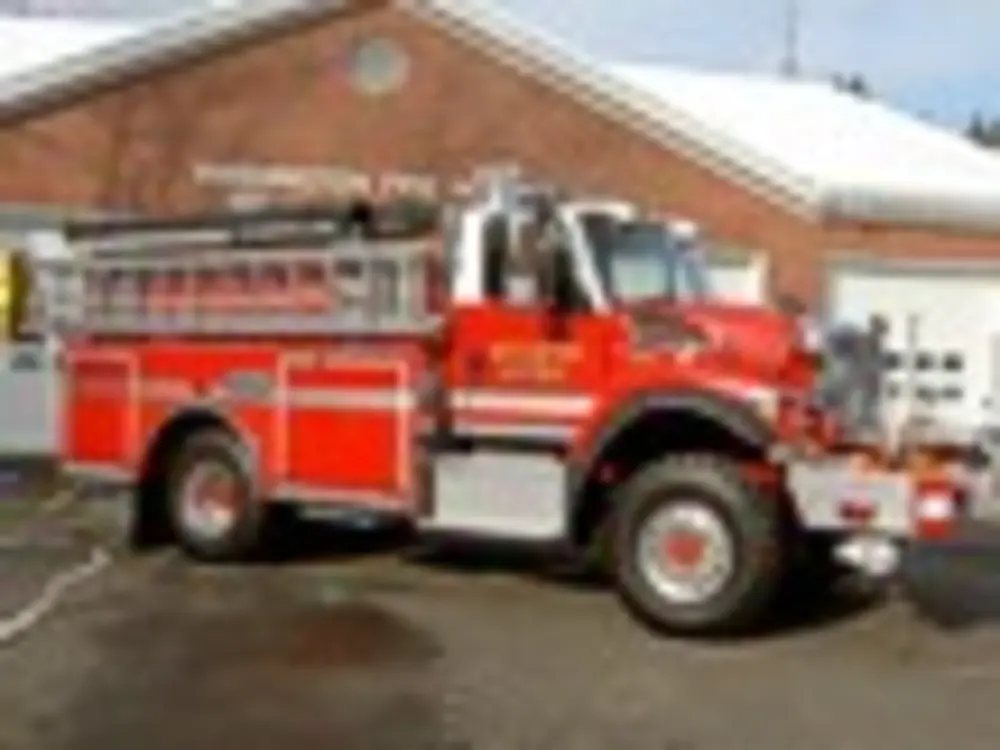 Exterior view of small fire truck showing cab, body compartments, and wheel/tire area.