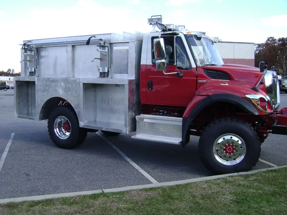 Exterior view of small fire truck showing cab, body compartments, and wheel/tire area.