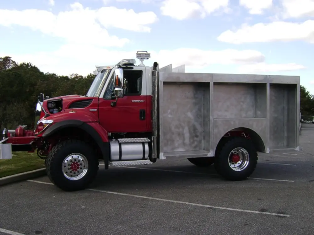 Exterior view of small fire truck showing cab, body compartments, and wheel/tire area.