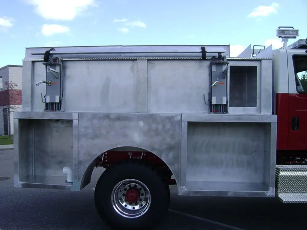 Exterior view of small fire truck showing cab, body compartments, and wheel/tire area.