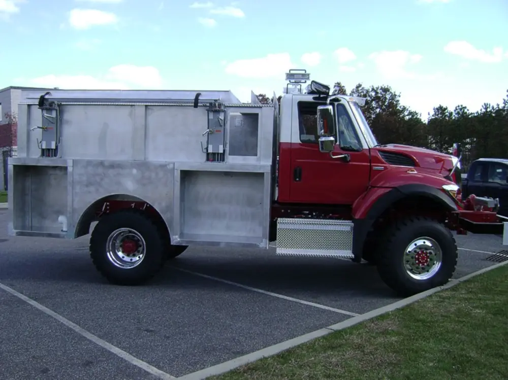 Exterior view of small fire truck showing cab, body compartments, and wheel/tire area.