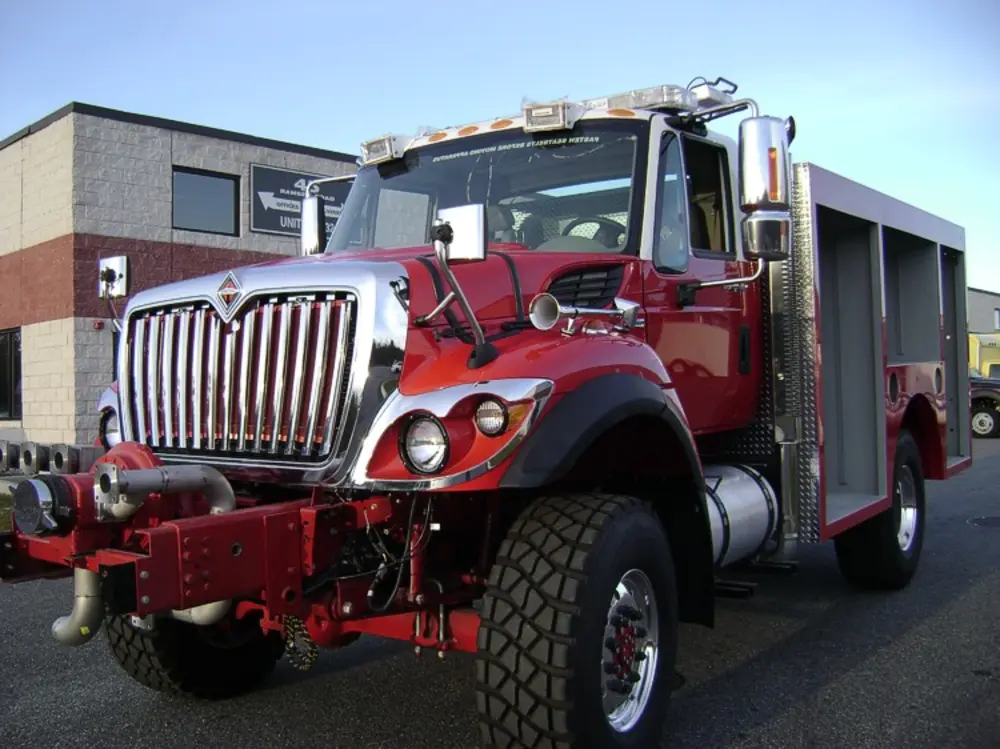 Exterior view of small fire truck showing cab, body compartments, and wheel/tire area.