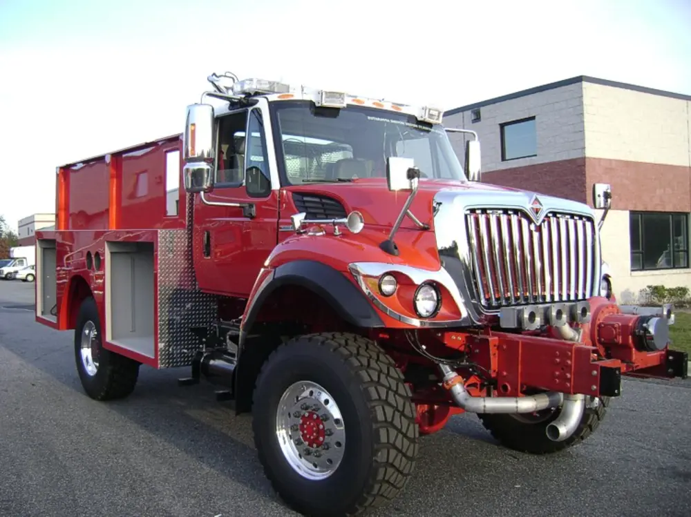 Exterior view of small fire truck showing cab, body compartments, and wheel/tire area.