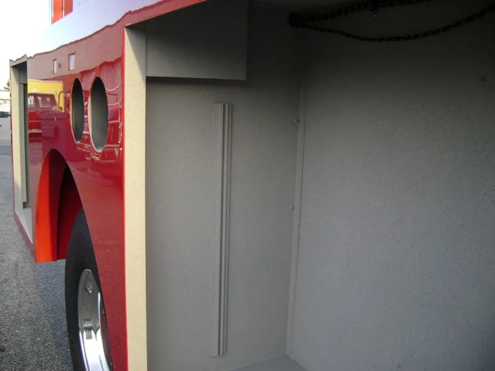 Exterior view of small fire truck showing cab, body compartments, and wheel/tire area.