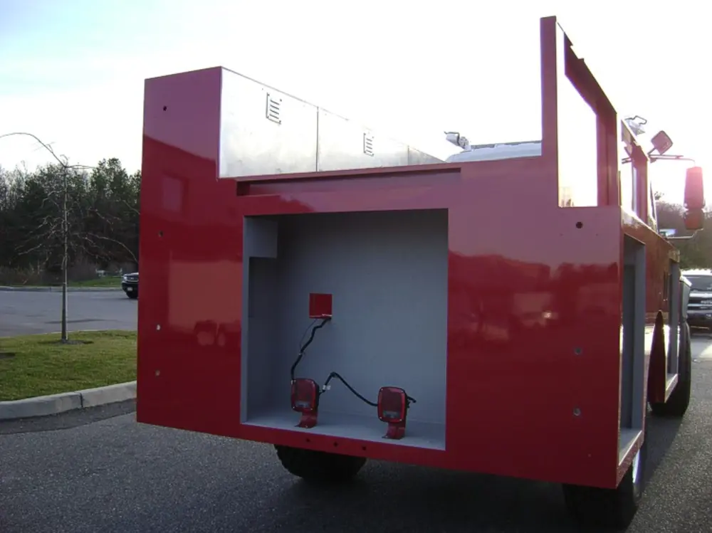 Exterior view of small fire truck showing cab, body compartments, and wheel/tire area.