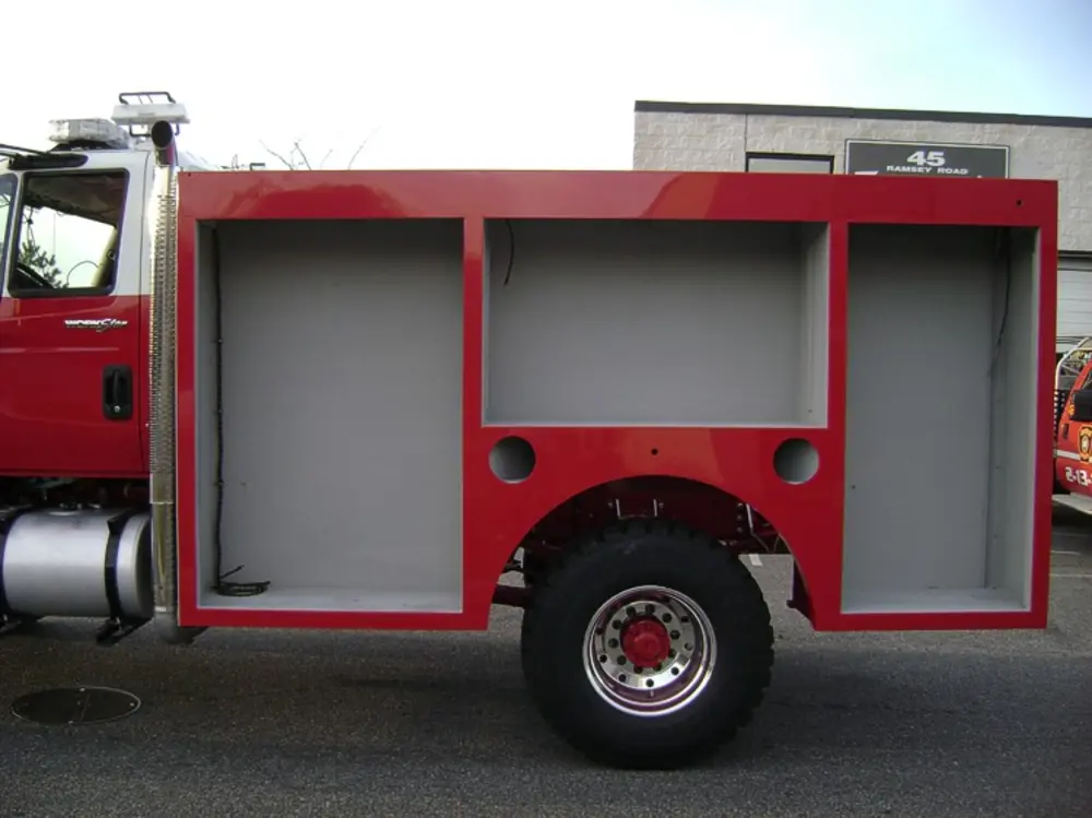 Exterior view of small fire truck showing cab, body compartments, and wheel/tire area.