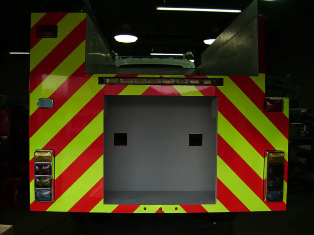 Exterior view of small fire truck showing cab, body compartments, and wheel/tire area.