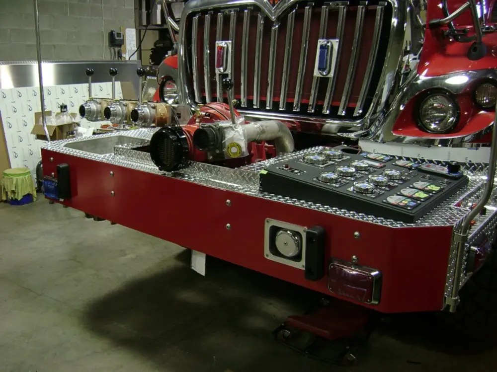 Exterior view of small fire truck showing cab, body compartments, and wheel/tire area.