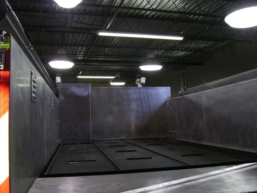 Exterior view of small fire truck showing cab, body compartments, and wheel/tire area.