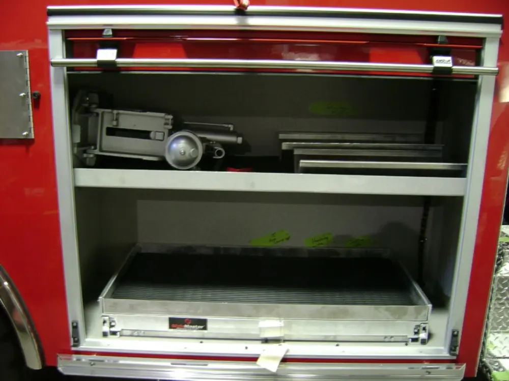 Exterior view of small fire truck showing cab, body compartments, and wheel/tire area.