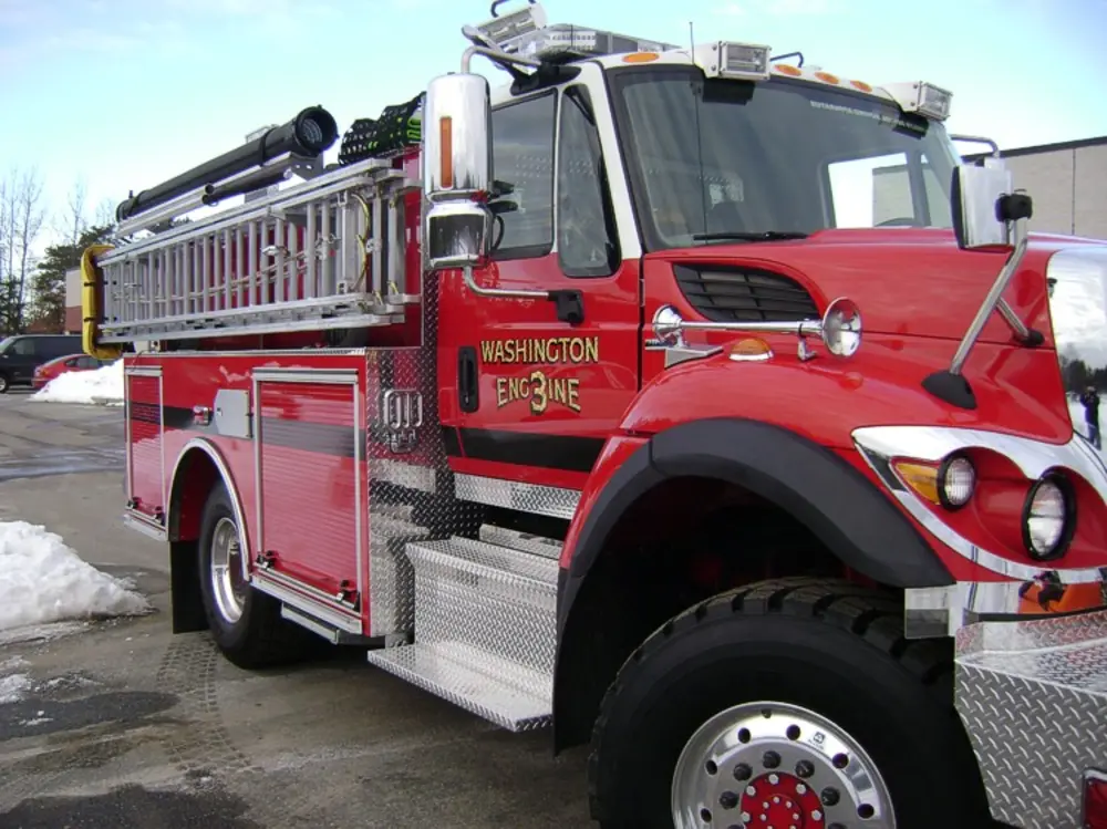 Exterior view of small fire truck showing cab, body compartments, and wheel/tire area.