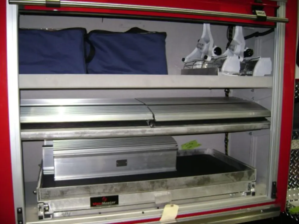 Exterior view of small fire truck showing cab, body compartments, and wheel/tire area.