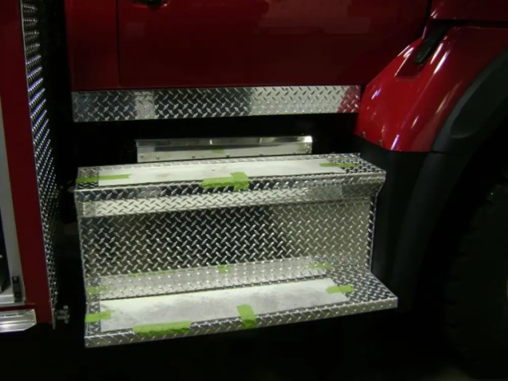 Exterior view of small fire truck showing cab, body compartments, and wheel/tire area.