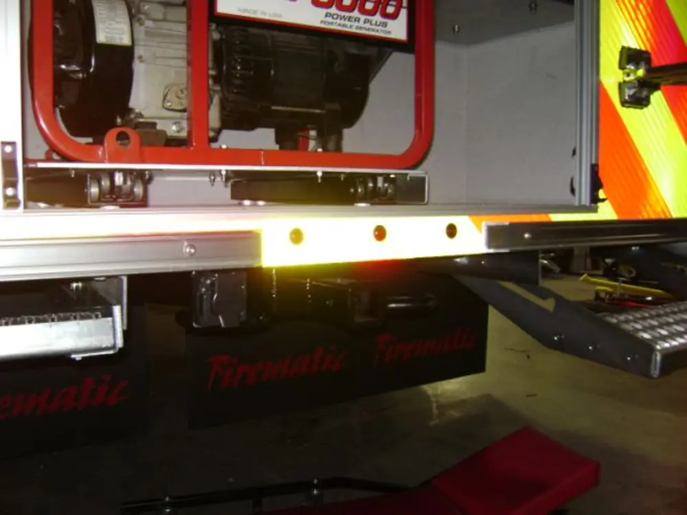 Exterior view of small fire truck showing cab, body compartments, and wheel/tire area.