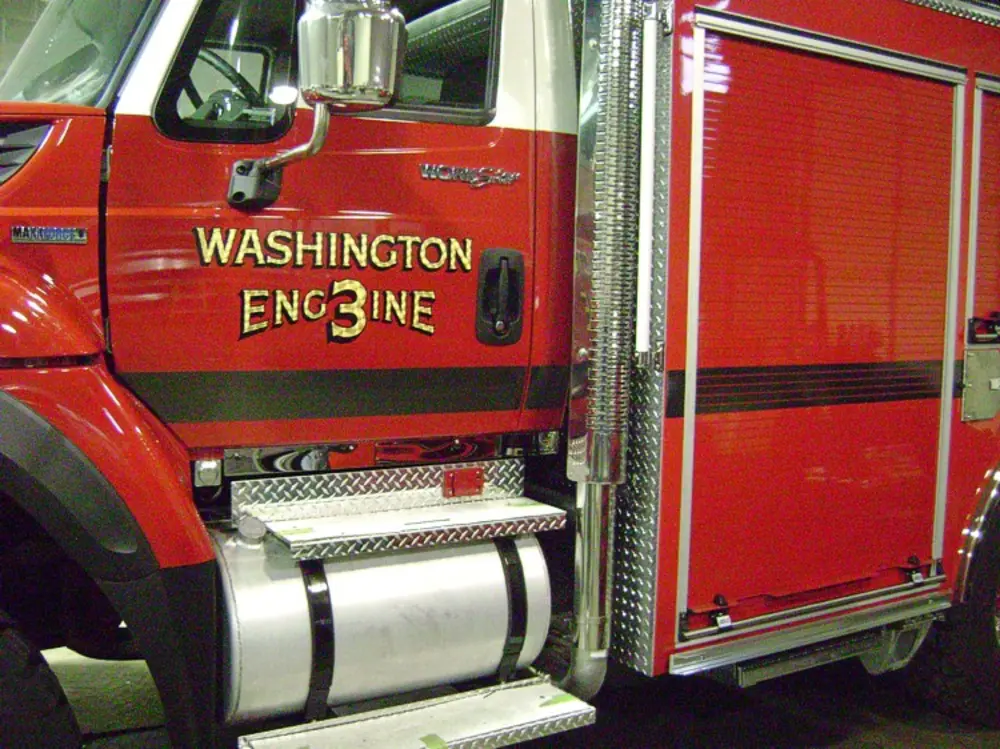 Exterior view of small fire truck showing cab, body compartments, and wheel/tire area.