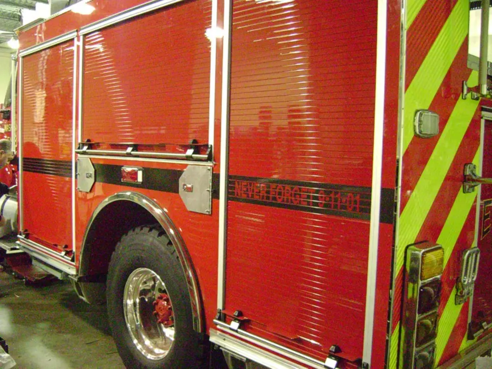 Exterior view of small fire truck showing cab, body compartments, and wheel/tire area.