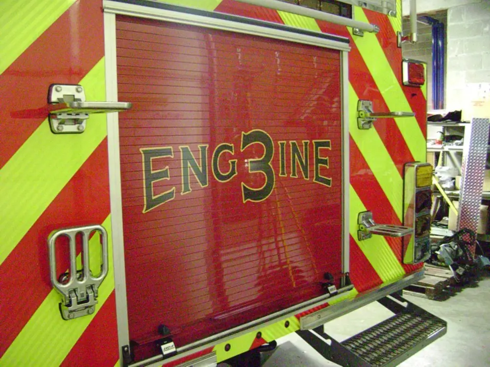 Exterior view of small fire truck showing cab, body compartments, and wheel/tire area.