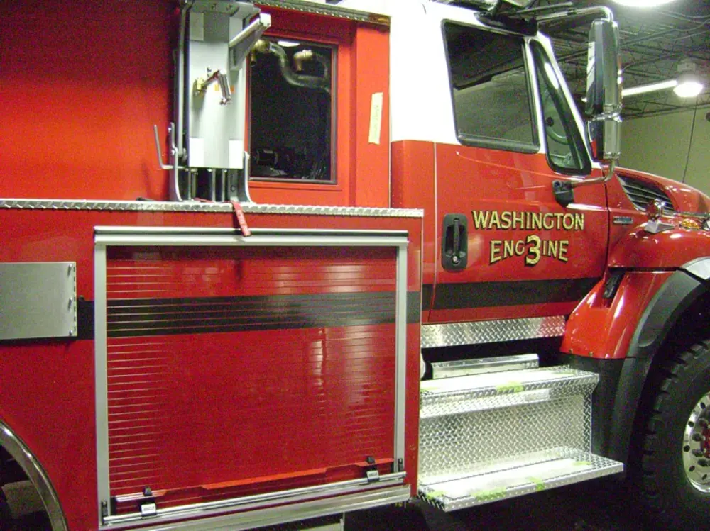 Exterior view of small fire truck showing cab, body compartments, and wheel/tire area.