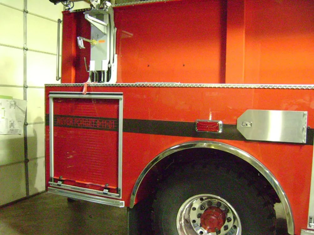 Exterior view of small fire truck showing cab, body compartments, and wheel/tire area.