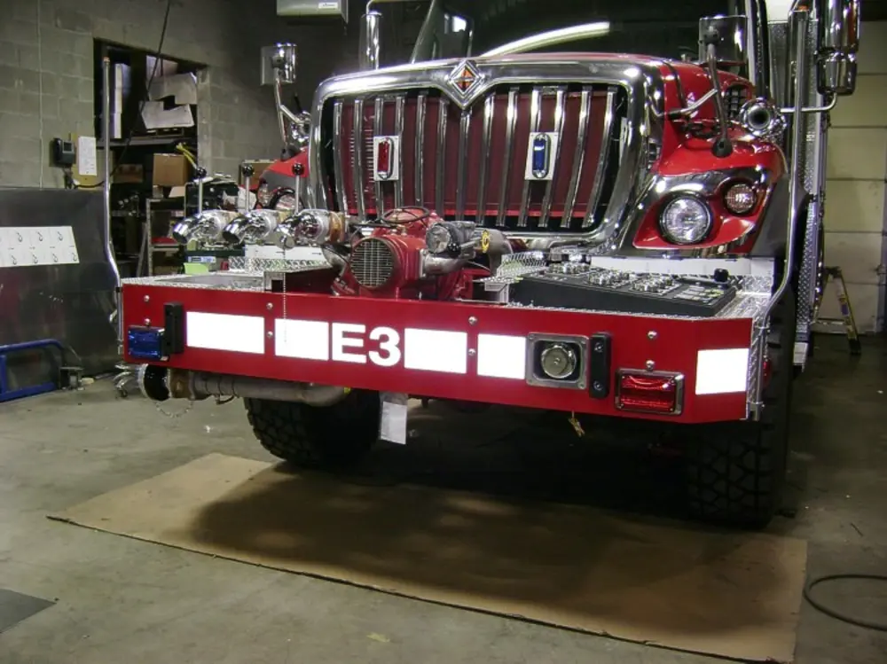 Exterior view of small fire truck showing cab, body compartments, and wheel/tire area.
