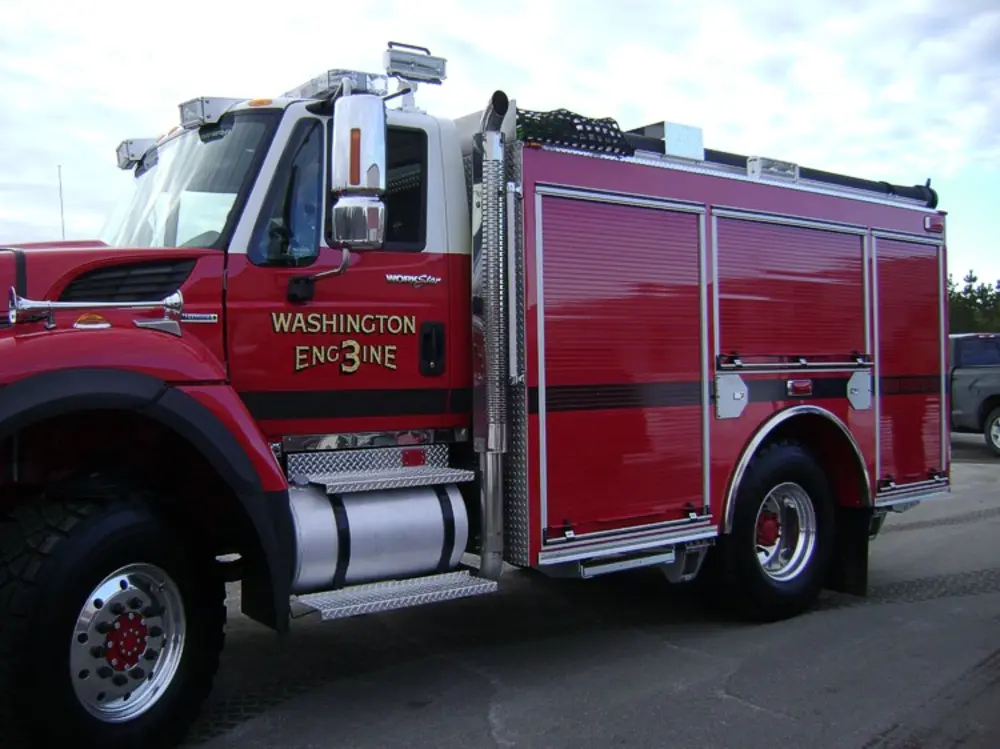 Exterior view of small fire truck showing cab, body compartments, and wheel/tire area.