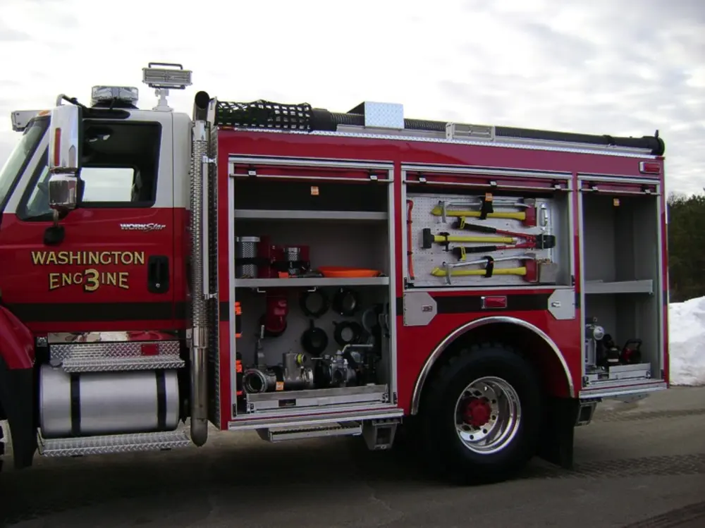 Exterior view of small fire truck showing cab, body compartments, and wheel/tire area.