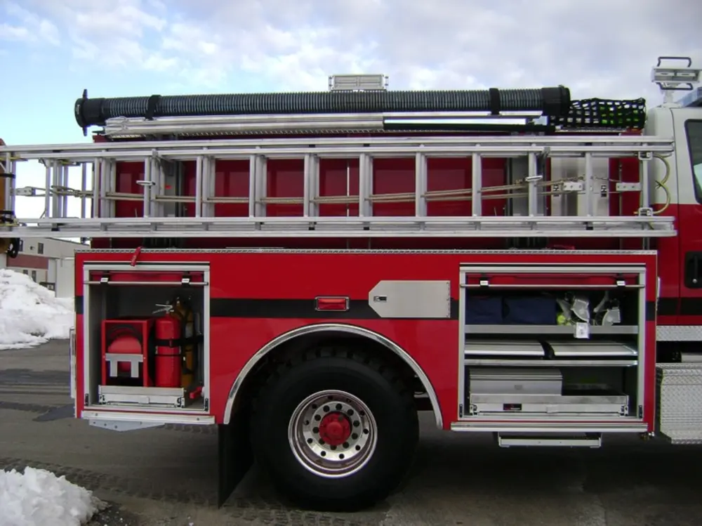 Exterior view of small fire truck showing cab, body compartments, and wheel/tire area.