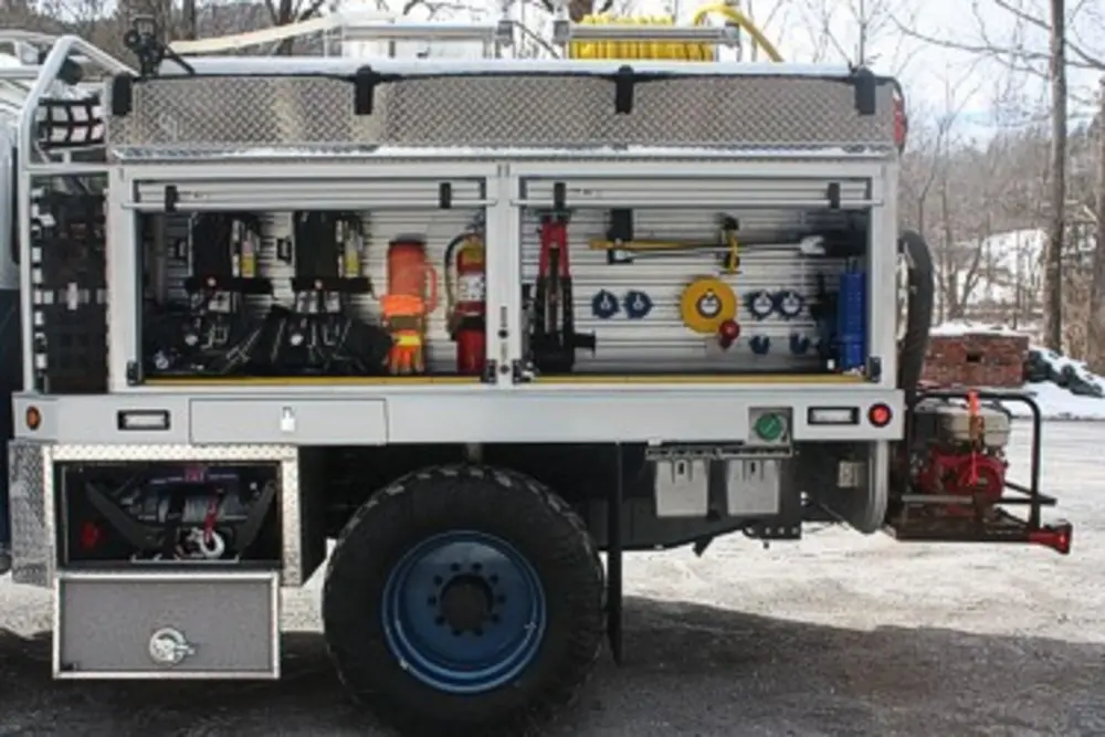 Exterior view of small fire truck showing cab, body compartments, and wheel/tire area.